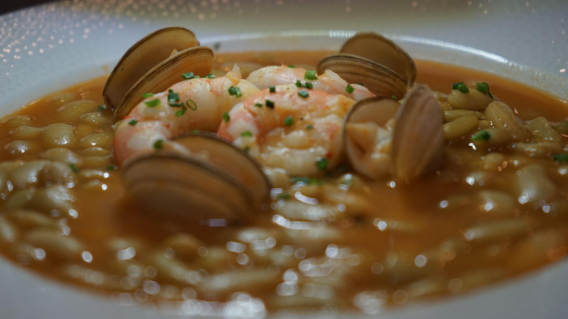 Un primer plano de un tazón de sopa con camarones y almejas en una mesa.