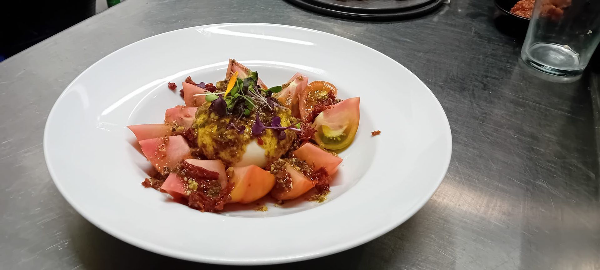 Un plato blanco cubierto de tomates y otras verduras sobre una mesa.