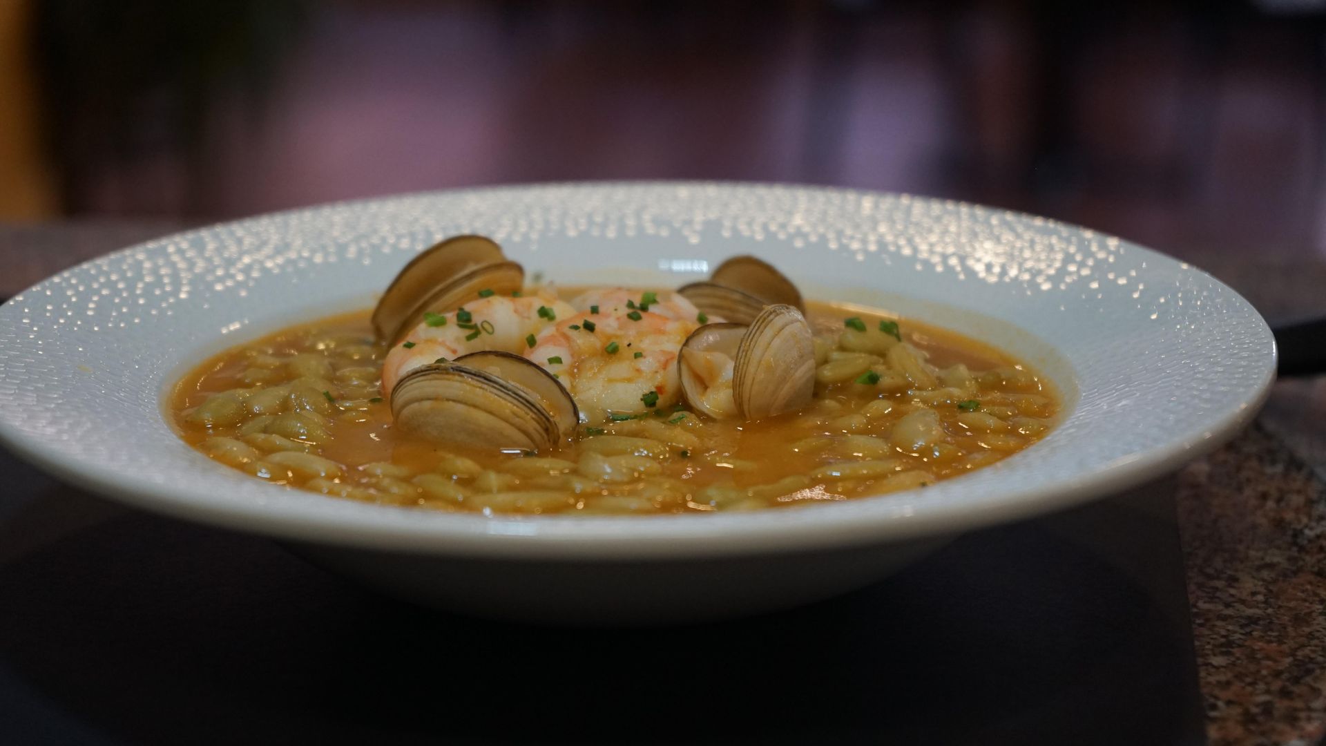 Un primer plano de un tazón de sopa con camarones y almejas en una mesa.