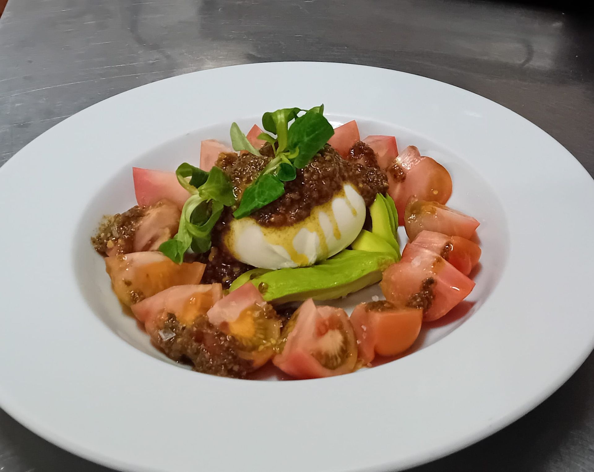 Un plato blanco cubierto con tomates y aguacate sobre una mesa.