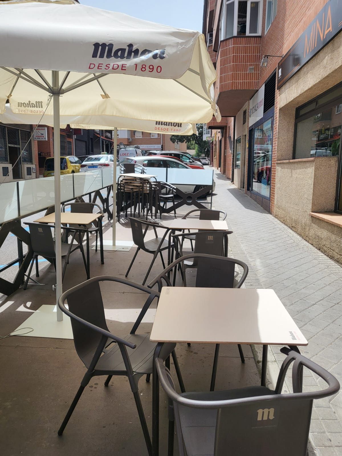 Una fila de mesas y sillas bajo una sombrilla en una acera.