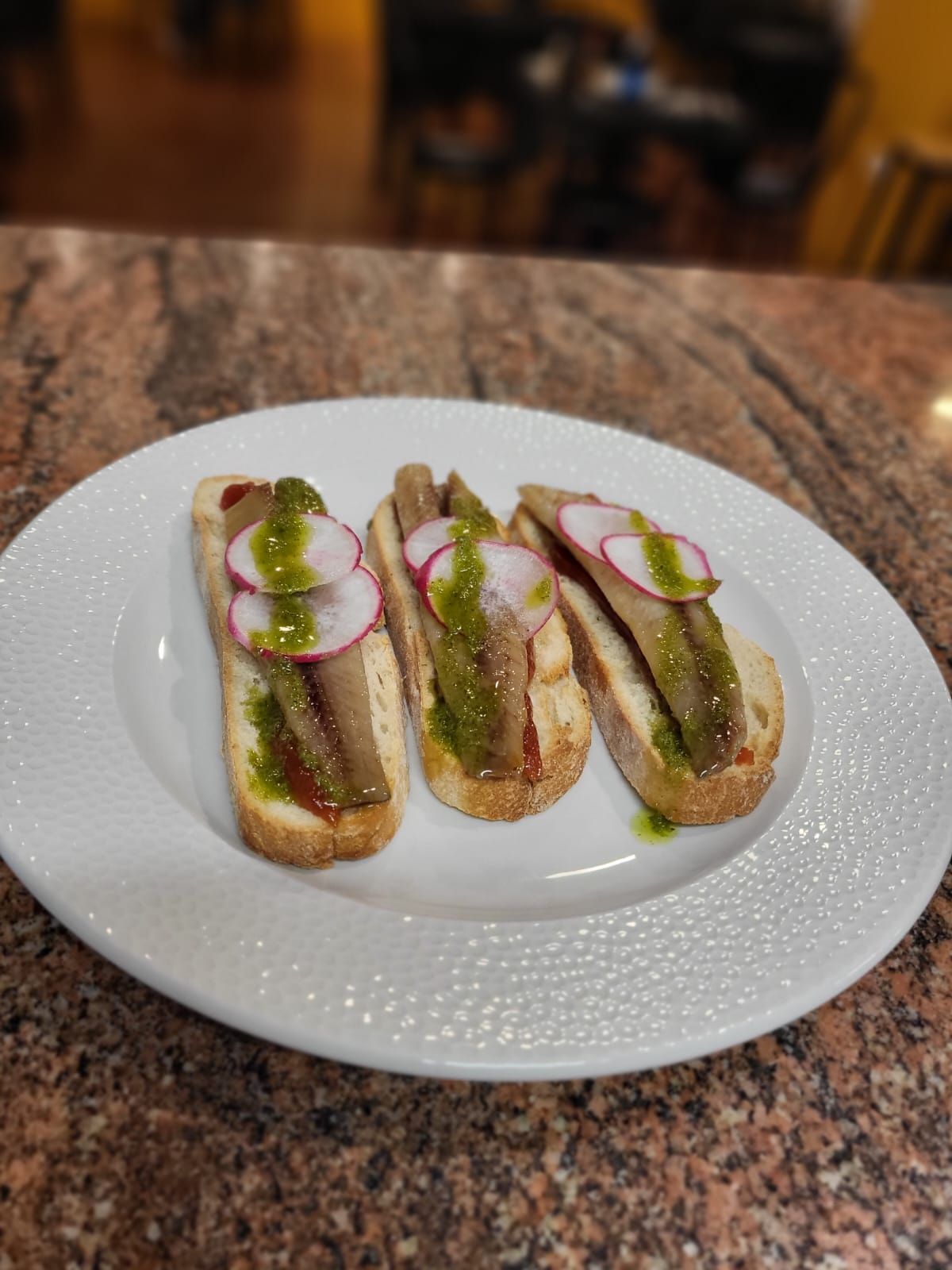 Un plato blanco cubierto con tres sándwiches sobre una encimera de granito.