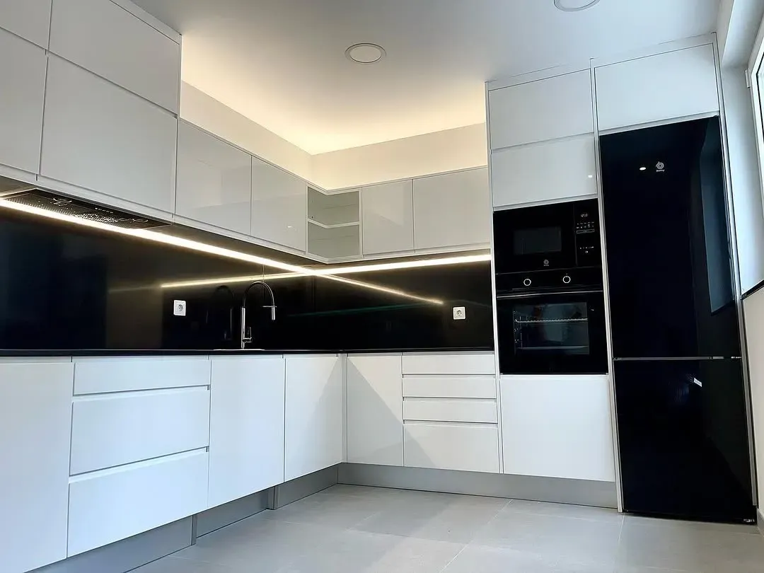 Una cocina moderna con armarios blancos, salpicadero y electrodomésticos en negro brillante