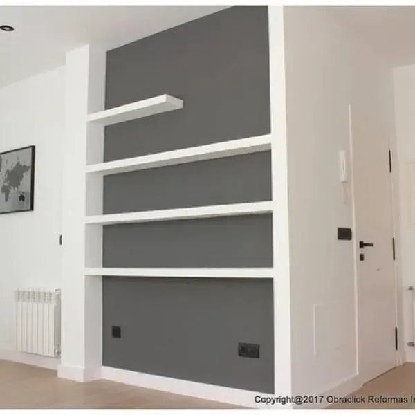 Una pared interior moderna pintada en gris carbón con cuatro estantes blancos empotrados de diferentes anchos.