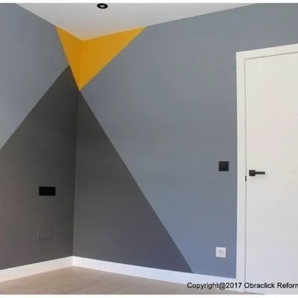 Una pared de esquina interior pintada con triángulos geométricos amarillos, gris oscuro y gris claro
