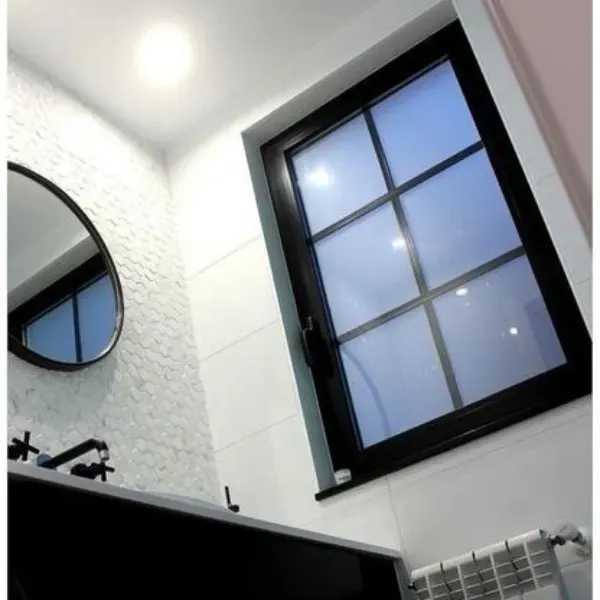 Un baño moderno con una ventana de marco negro, un espejo redondo, paredes blancas texturizadas y un tocador negro.