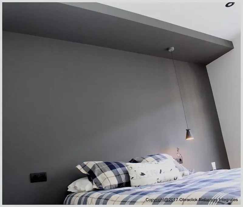 Dormitorio moderno con una pared decorativa de color gris oscuro, una colcha a cuadros y una lámpara colgante individual.
