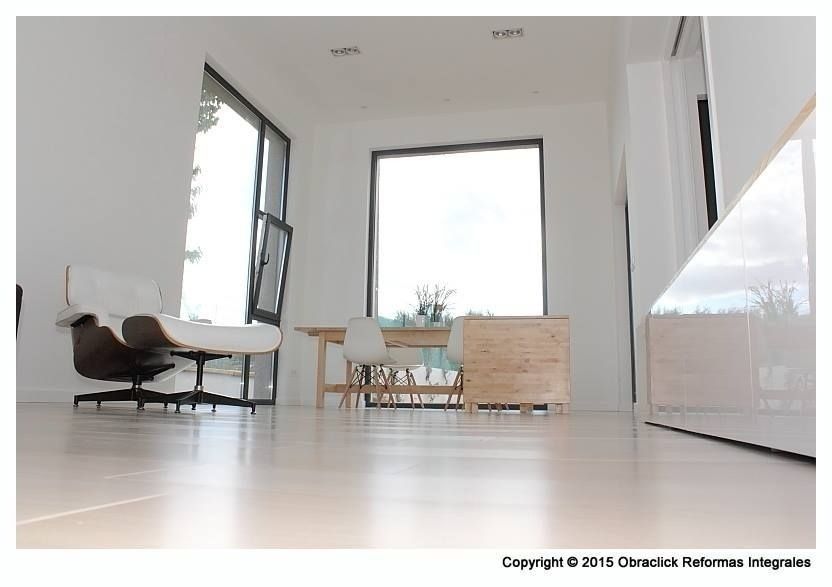 Una habitación minimalista con paredes blancas y suelo de madera clara, que cuenta con un sillón y un juego de comedor