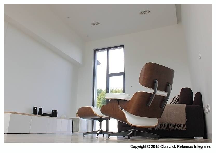 En un salón minimalista de paredes blancas, un sillón y un reposapiés de estilo Eames moderno
