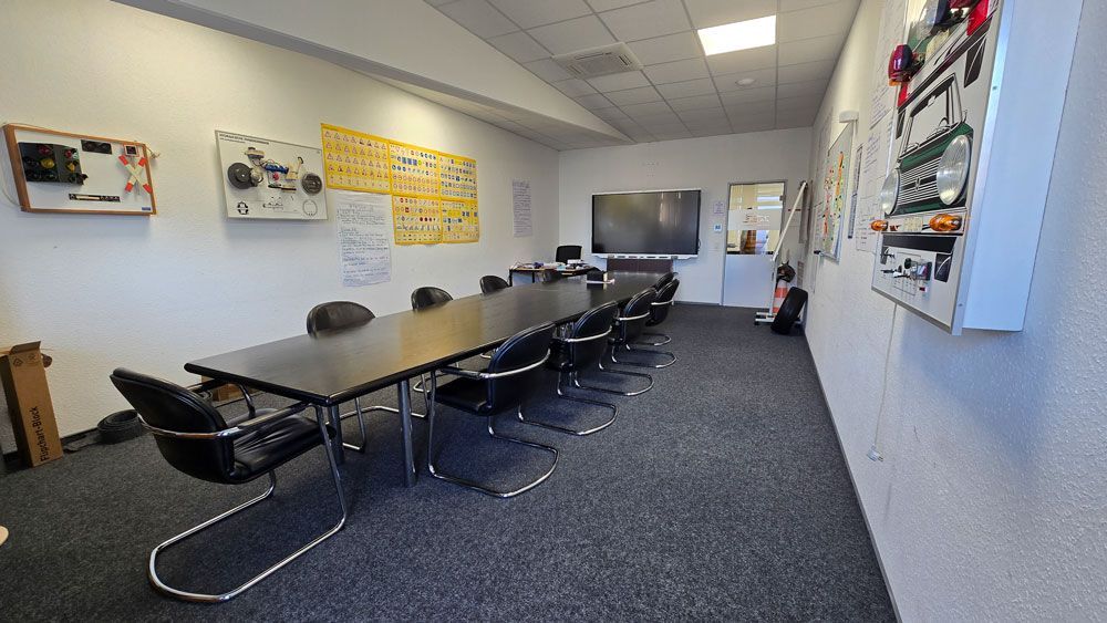 Konferenzraum mit langem schwarzen Tisch, Stühlen und Lehrtafeln an den Wänden.