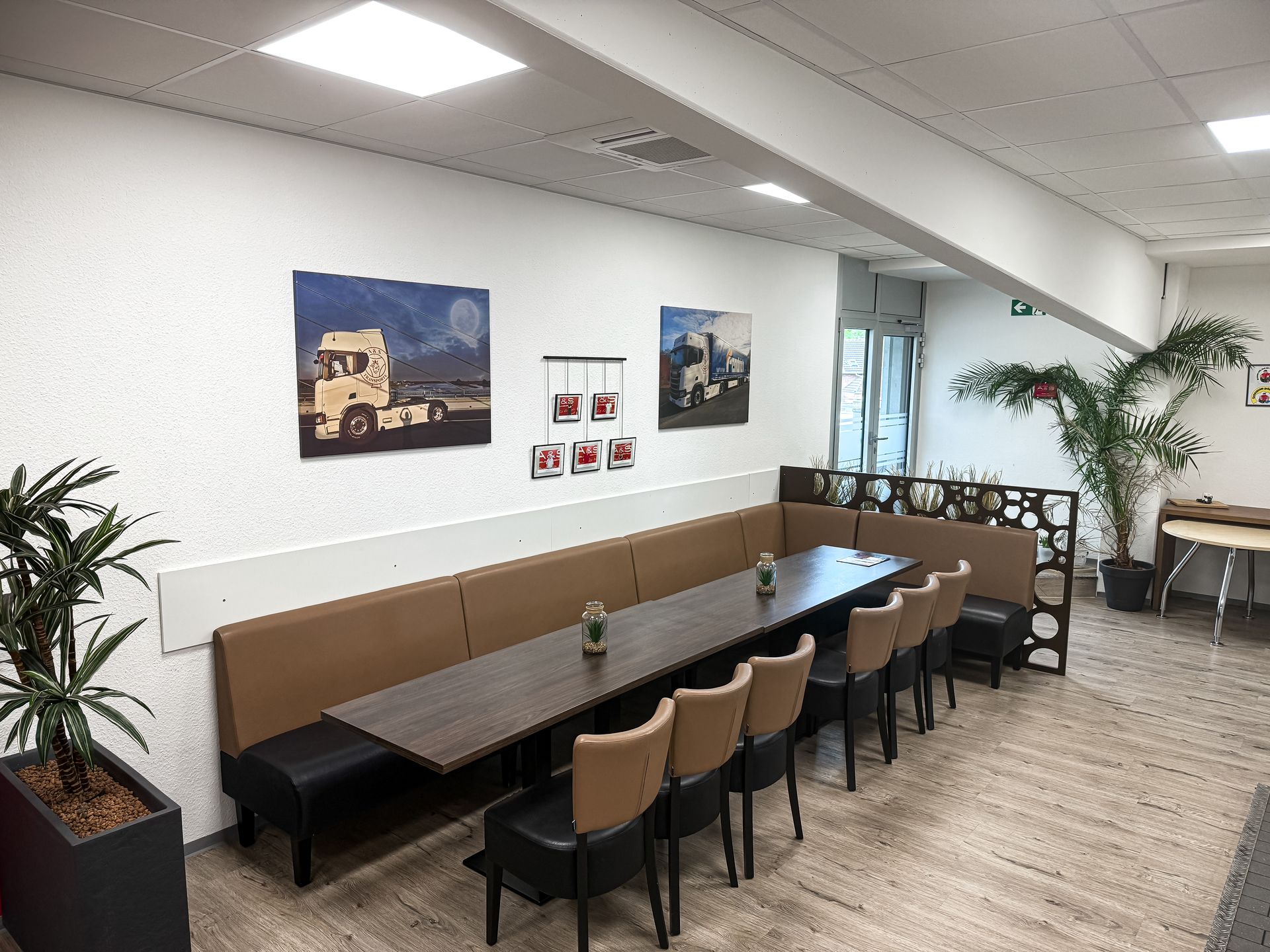 Essbereich mit langem Tisch, brauner Bank, Stühlen, LKW-Kunst, Topfpflanzen.