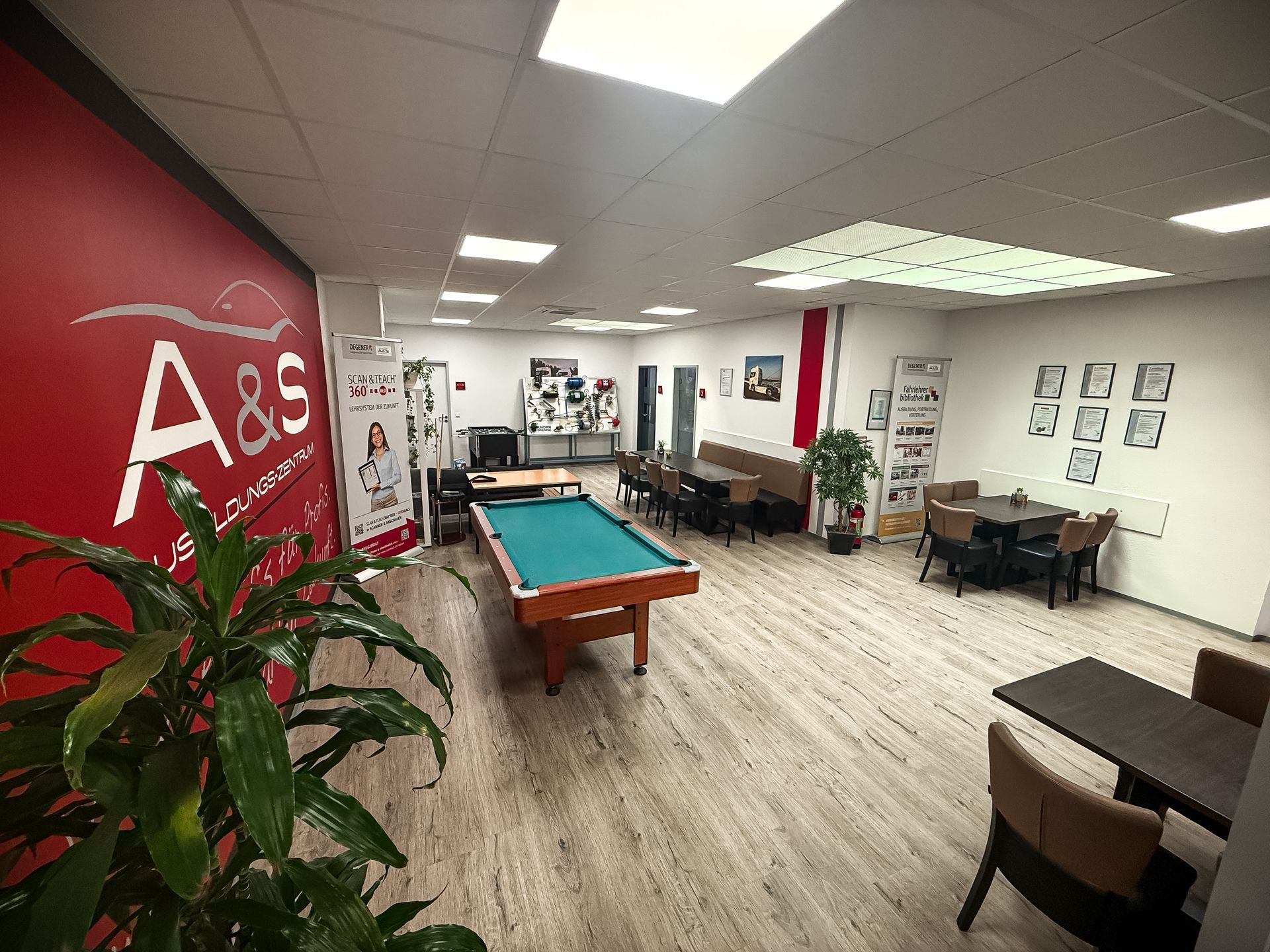 Inneneinrichtung mit Billardtisch, Sitzecken und einer roten Wand mit Logo.