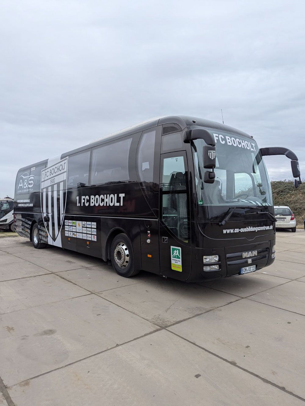 Auf einem Parkplatz steht ein schwarz-weißer Bus.