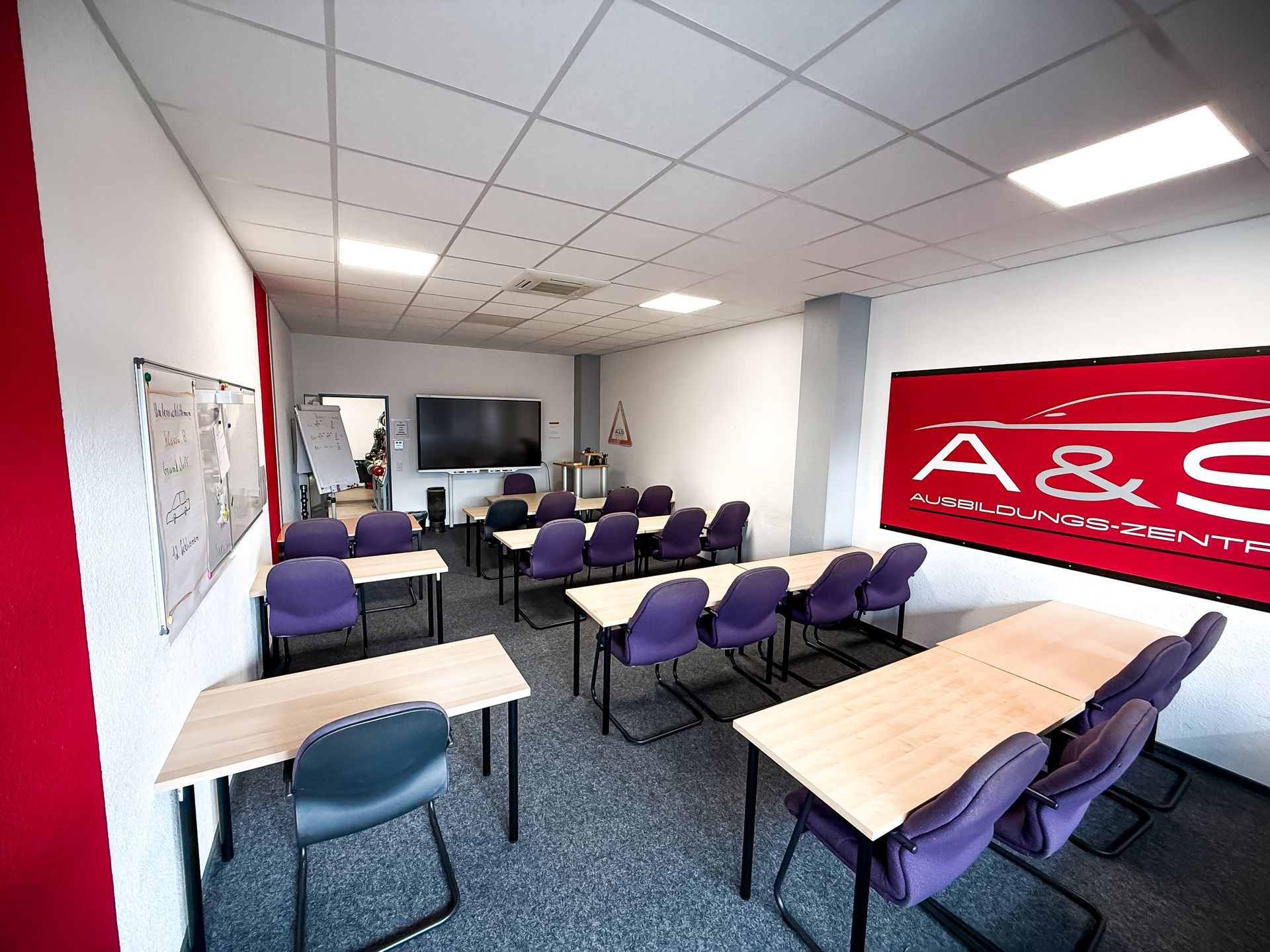 Ein Klassenzimmer mit lila Stühlen und Tischen und einem Schild mit der Aufschrift „A & S“ an der Wand.