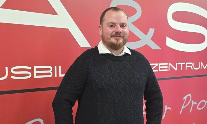 Ein Mann steht mit verschränkten Armen vor einer roten Wand.