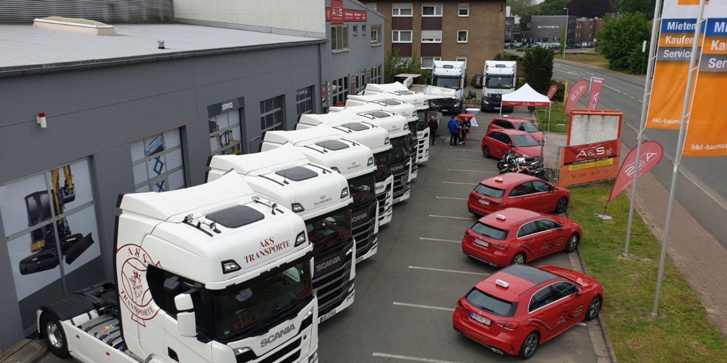 Vor einem Gebäude parken mehrere Lastwagen und Autos.