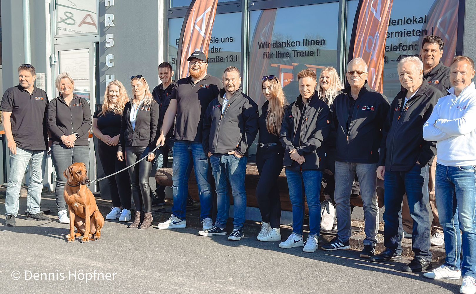 Eine Gruppe von Menschen steht mit einem Hund an der Leine vor einem Gebäude.