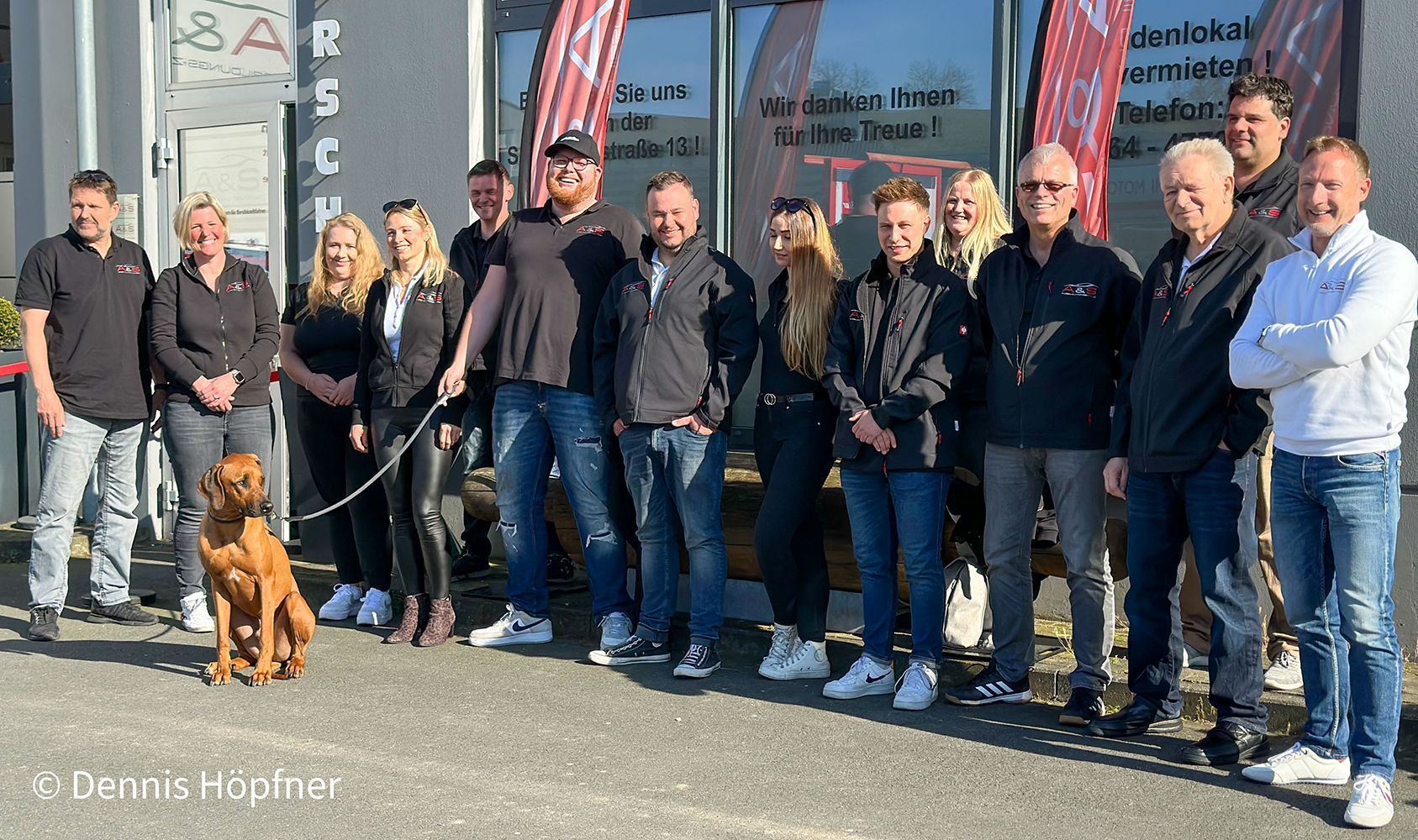 Eine Gruppe von Menschen steht mit einem Hund an der Leine nebeneinander.