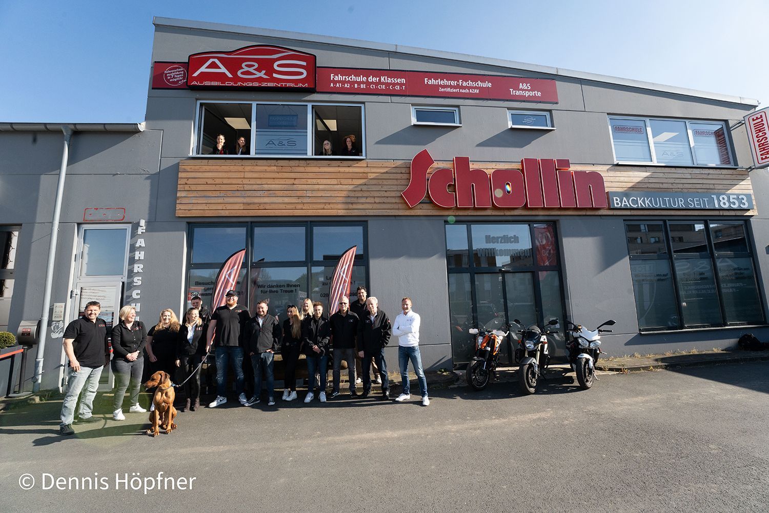 Eine Gruppe von Menschen steht vor einem Gebäude mit der Aufschrift „A & S“