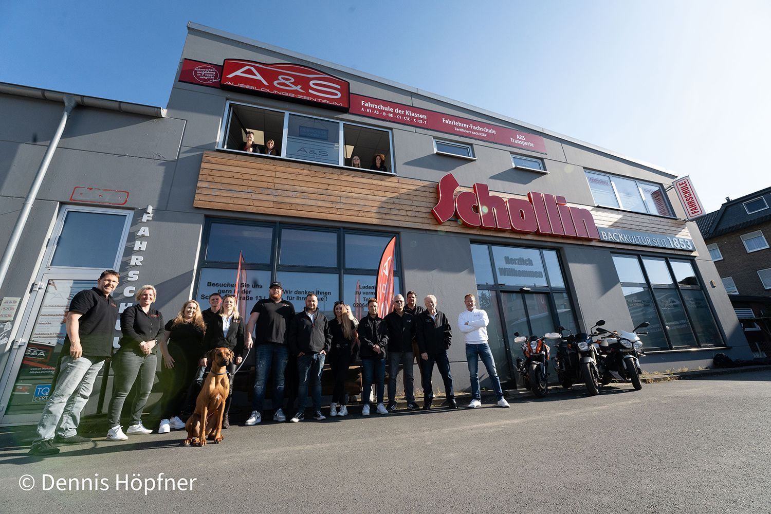 Eine Gruppe von Menschen und ein Hund posieren vor einem Gebäude für ein Foto.