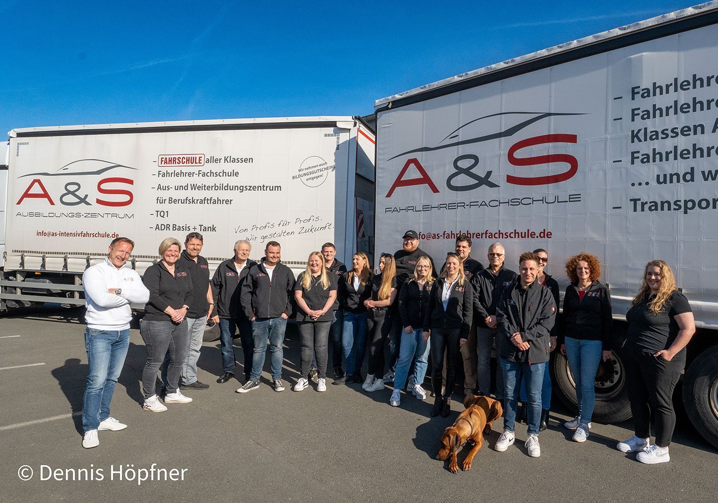 Gruppe von Menschen posiert mit zwei Lastwagen, Logo „A & S“. Sonniger Tag.