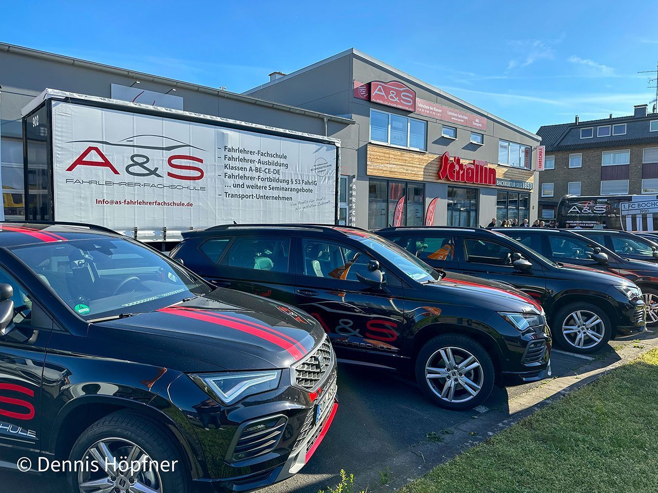 Vor einem Autohaus parken Autos, mit einem Schild mit der Aufschrift „A & S“ und einem blauen Himmel darüber.