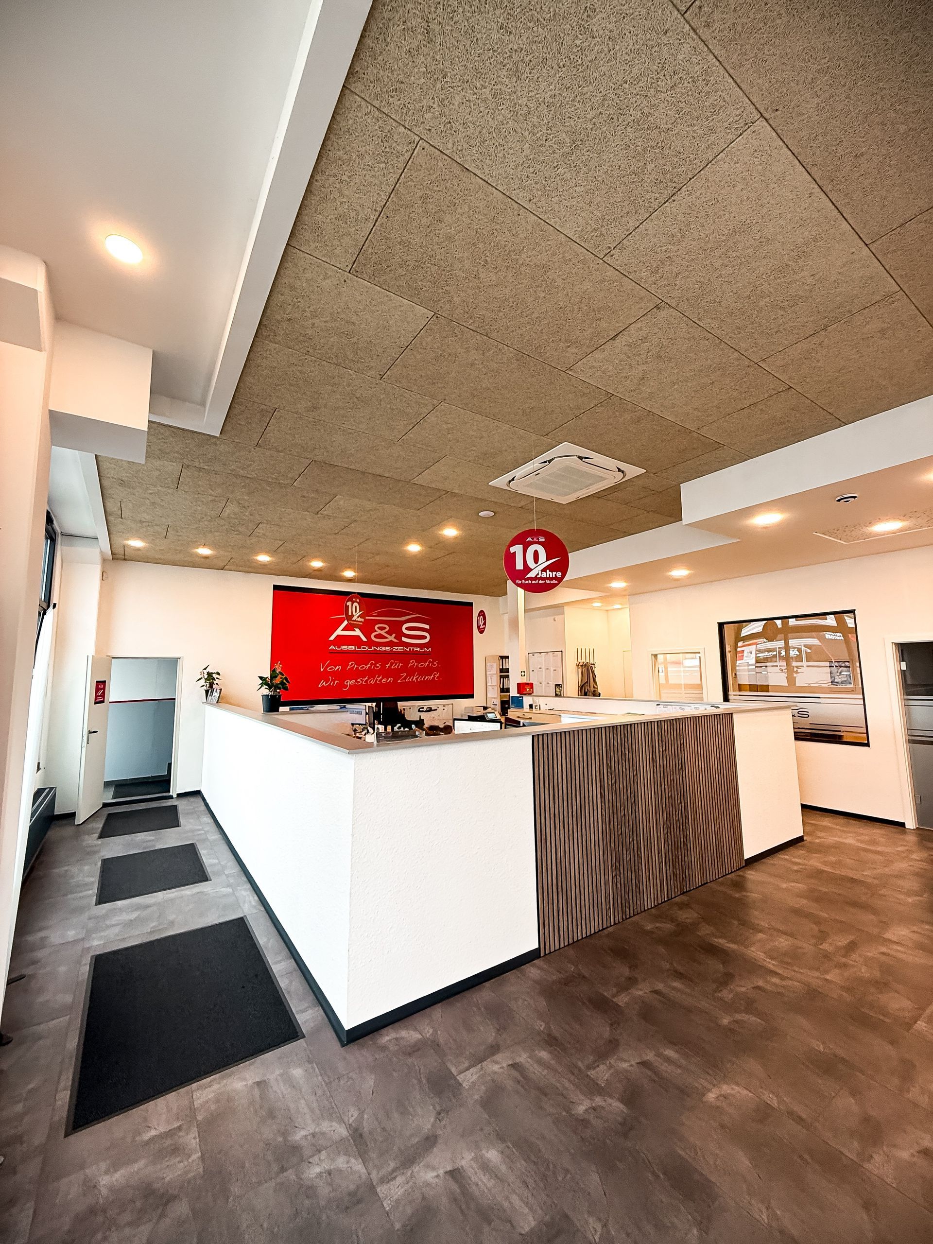 Empfangsbereich mit weißem und holzgemasertem Schreibtisch, rotem Logo und brauner Decke.