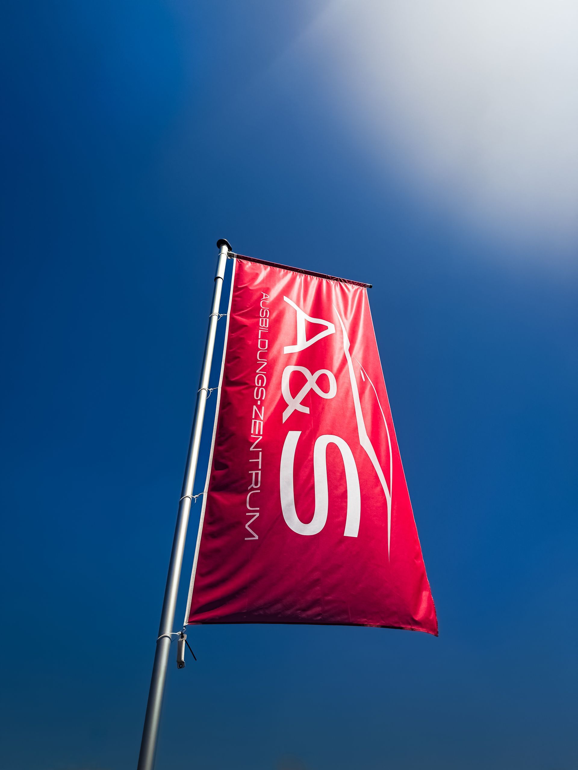 Rote Flagge mit weißem „A & S“-Logo vor strahlend blauem Himmel.