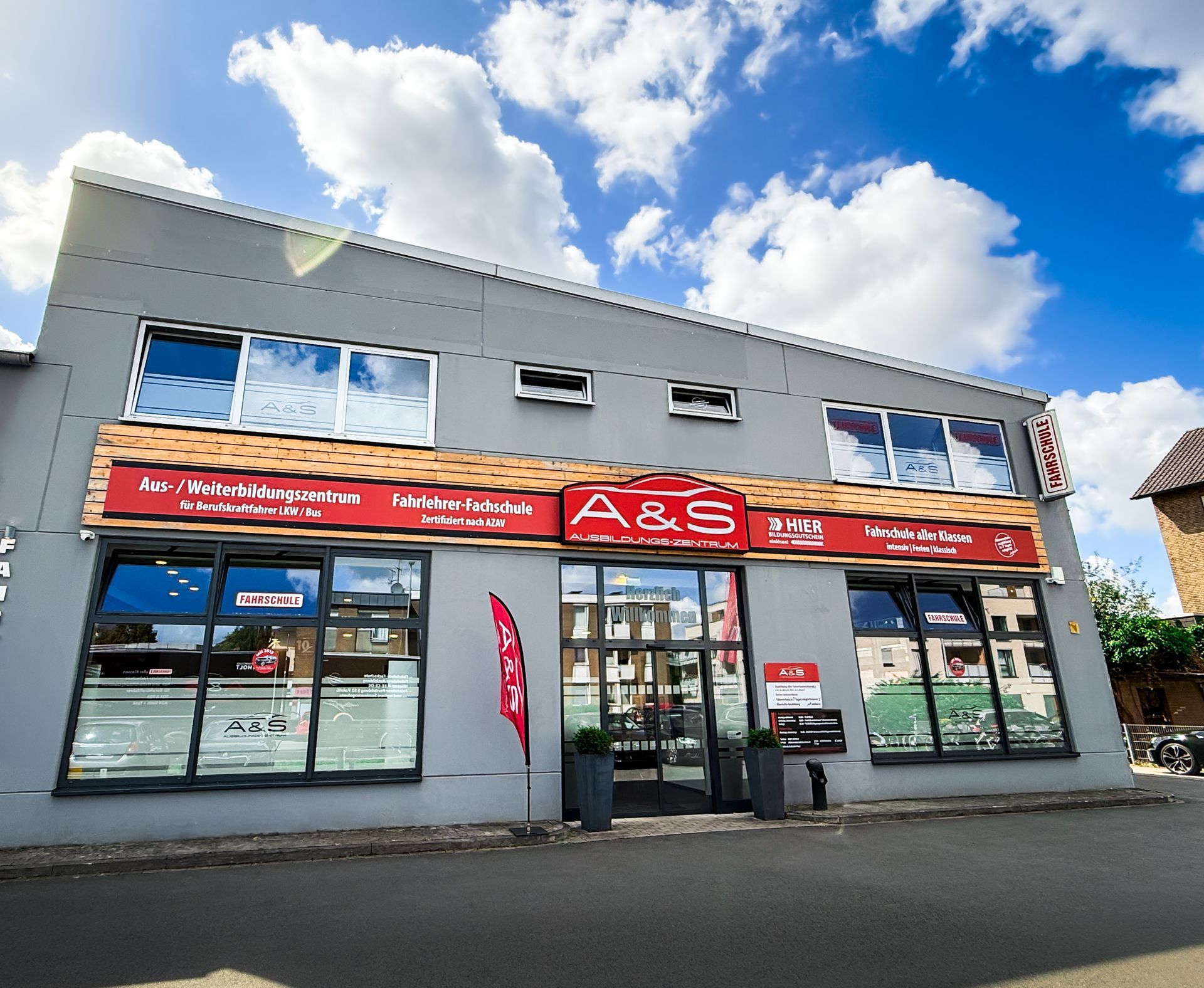 Außenansicht eines grauen Gebäudes mit großen Fenstern, der Firmenname A&S in roten Buchstaben, sonniger Tag.