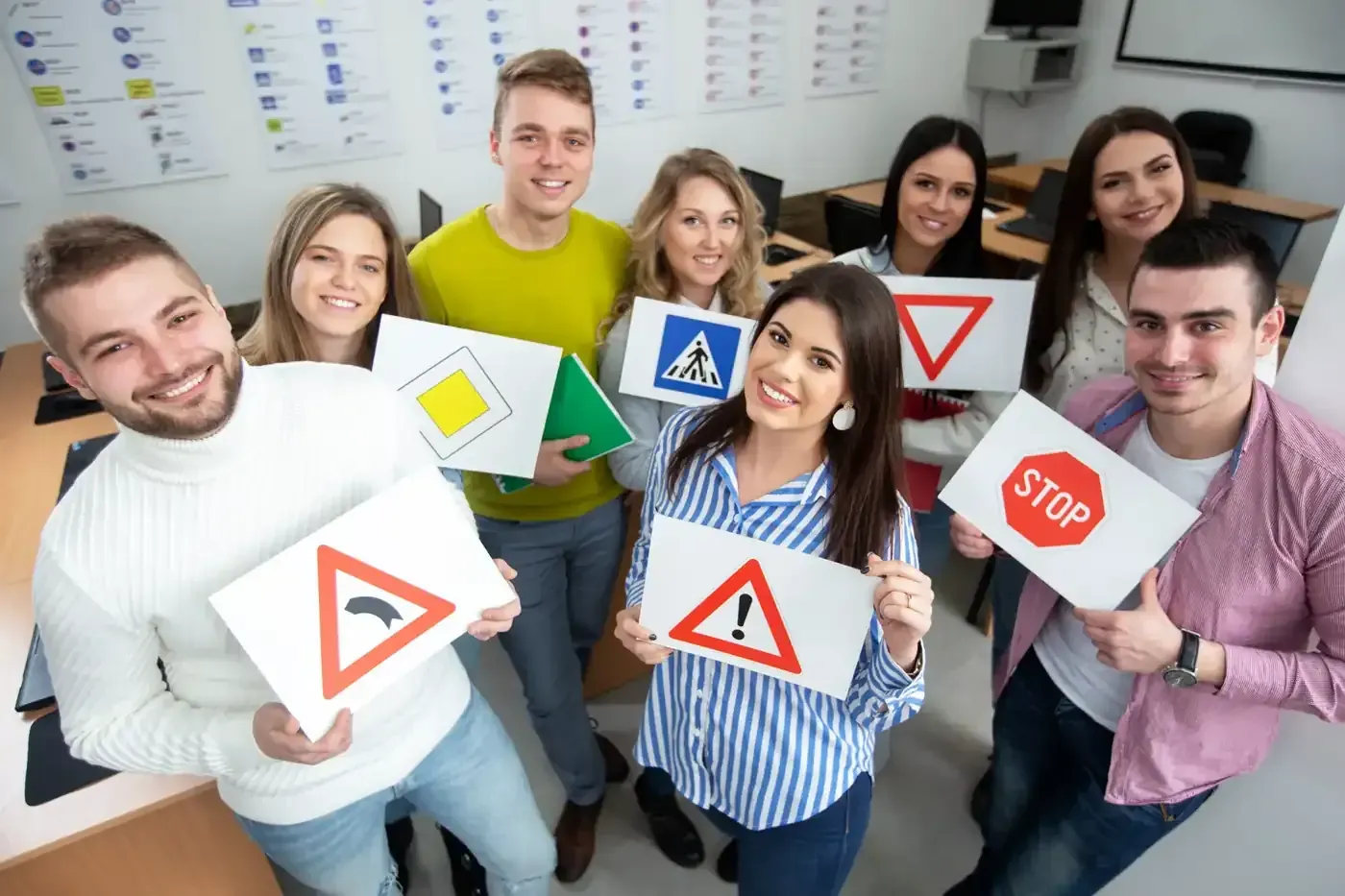 Grupo de personas sonriendo, sosteniendo señales de tráfico en un aula.