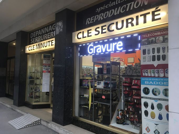 Façade de magasin avec enseignes lumineuses pour services de sécurité et gravure, visibles à travers la vitre la nuit.