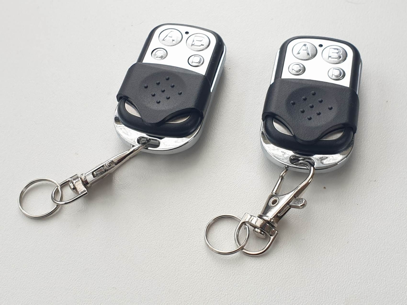 Deux télécommandes porte-clés noires et argentées sur une surface blanche