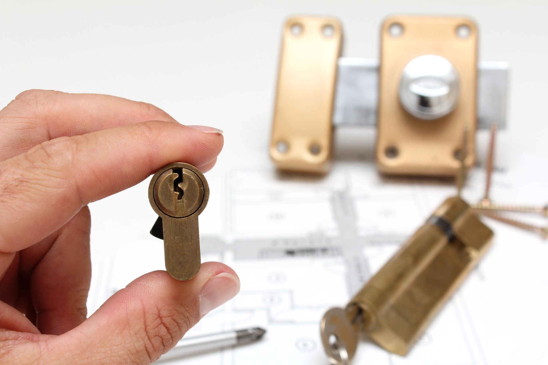 Main tenant une clé en laiton devant un cadenas et sa serrure flous sur fond blanc