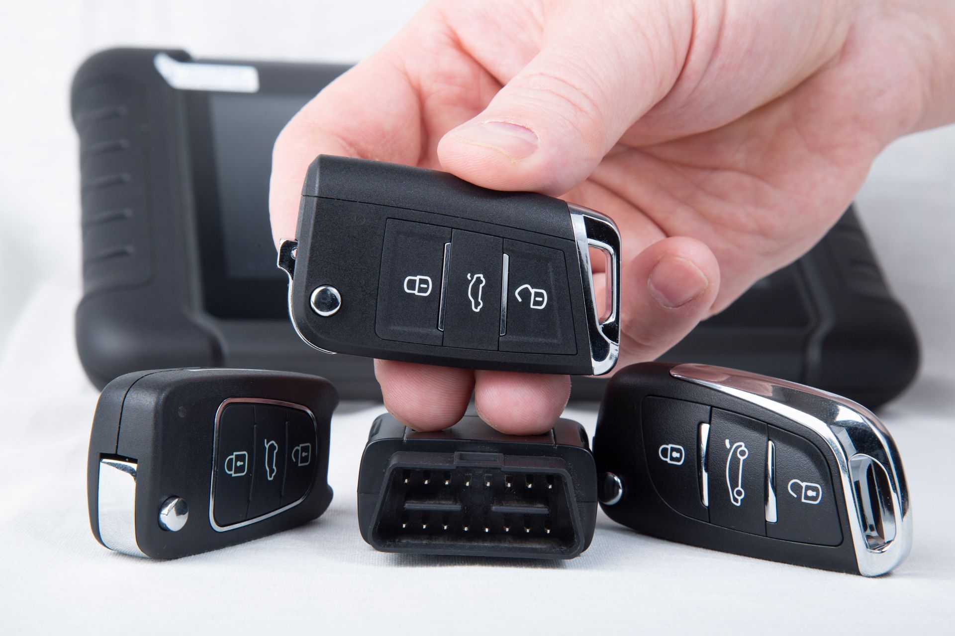 Main tenant une clé de voiture noire, avec d'autres clés et un récepteur d'entrée sans clé à proximité.