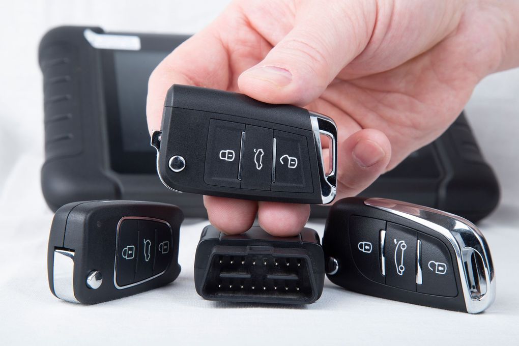 Main tenant une clé de voiture au-dessus de trois autres clés noires sur fond blanc