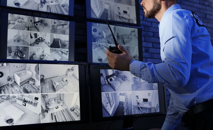 Guardia de seguridad monitoreando cámaras de vigilancia, sosteniendo un walkie-talkie.