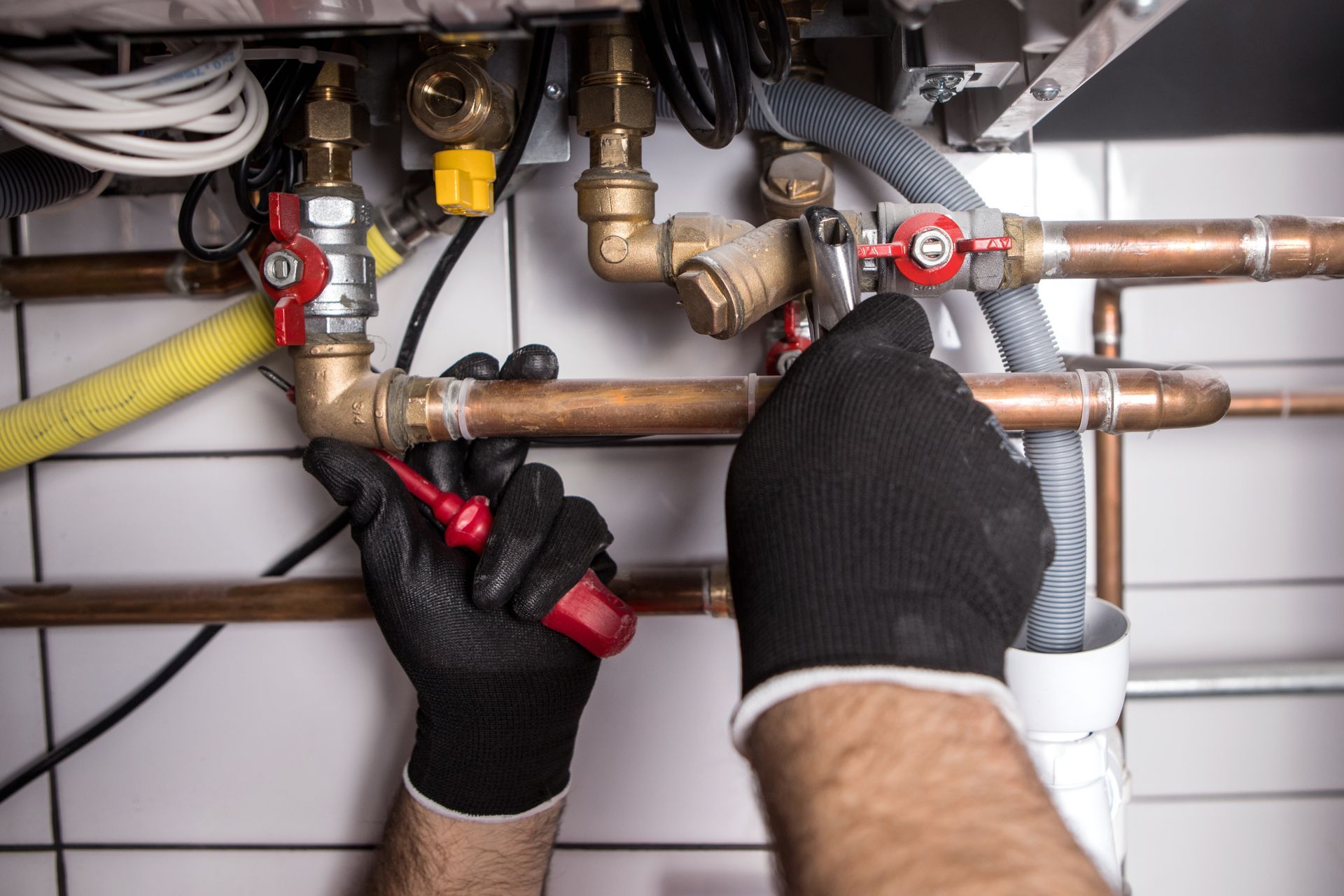 Mains gantées de noir travaillant sur des tuyaux et des vannes en cuivre