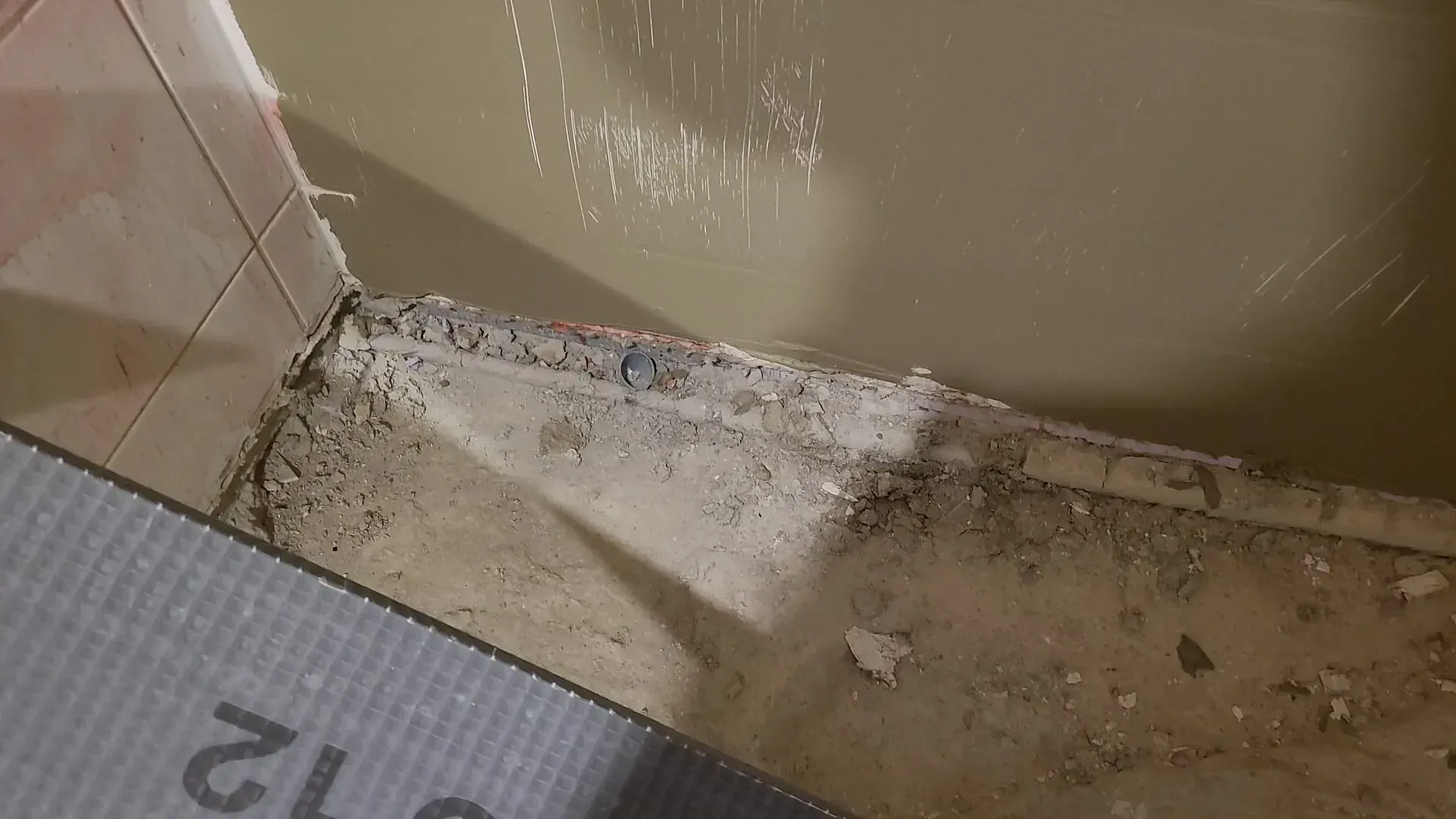 Schmutzige Badezimmerecke mit bröckelnder Wand, Schutt und einer unansehnlichen Fliesenkante