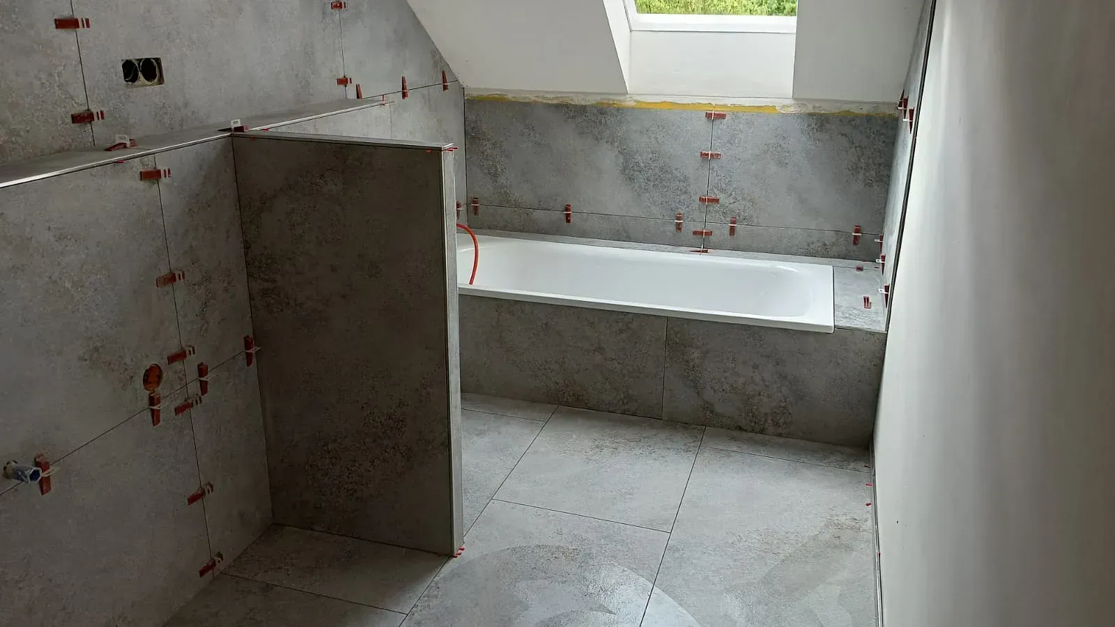 Kleines, unfertiges Badezimmer mit gefliestem Boden, Betonwänden und einer eingebauten Sitzbank unter einem Oberlicht.