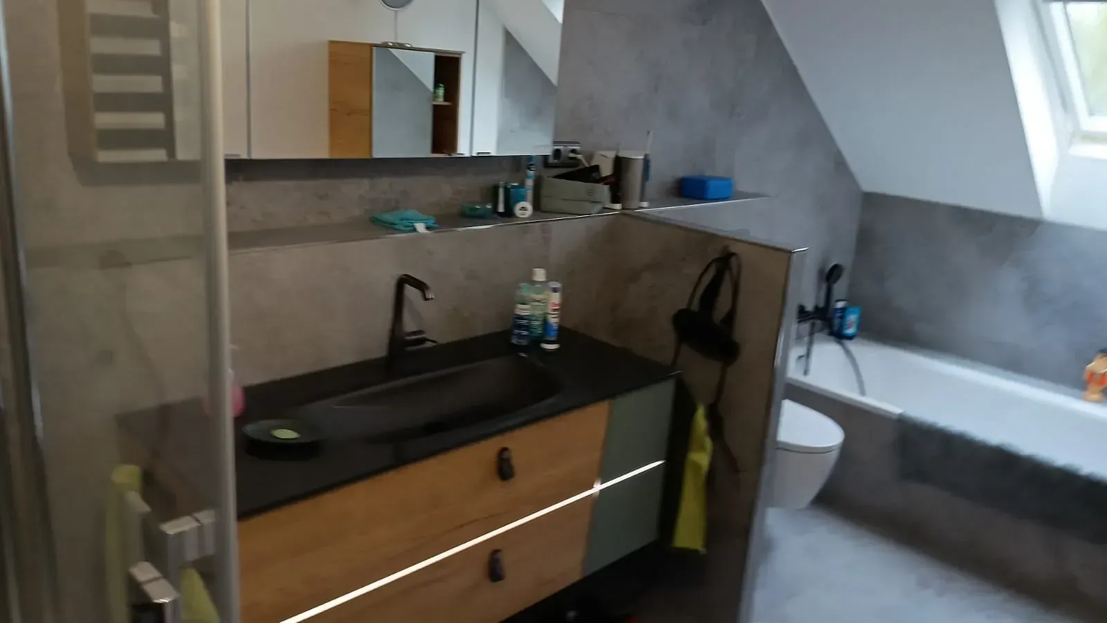 Kleines, modernes Badezimmer mit schwarzem Waschtisch, Waschbecken, Spiegel und Toilette unter einer Dachschräge.