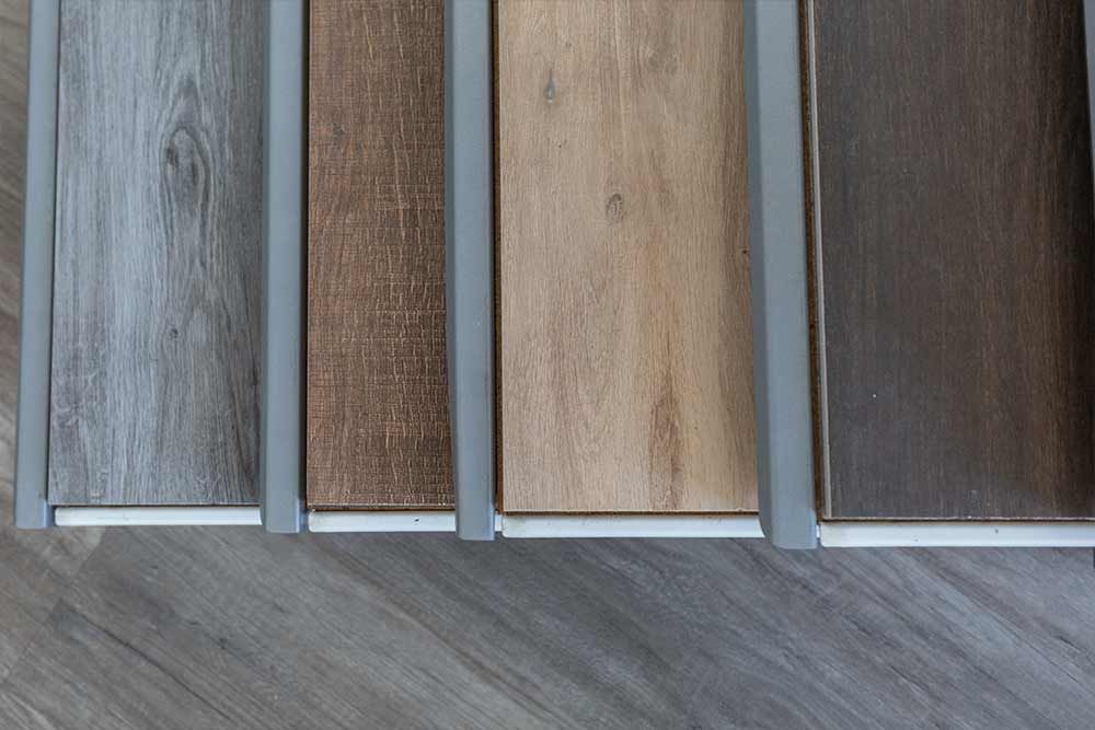 Vier Bodenmusterpaneele in Grau-, Braun-, Beige- und dunklen Holztönen auf einem grauen Boden
