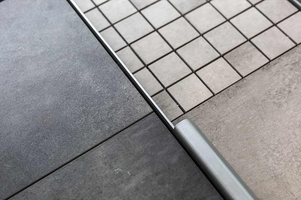 Diagonale Nahaufnahme eines dunklen und hellen Fliesenbodens mit einer Metallschwelle.