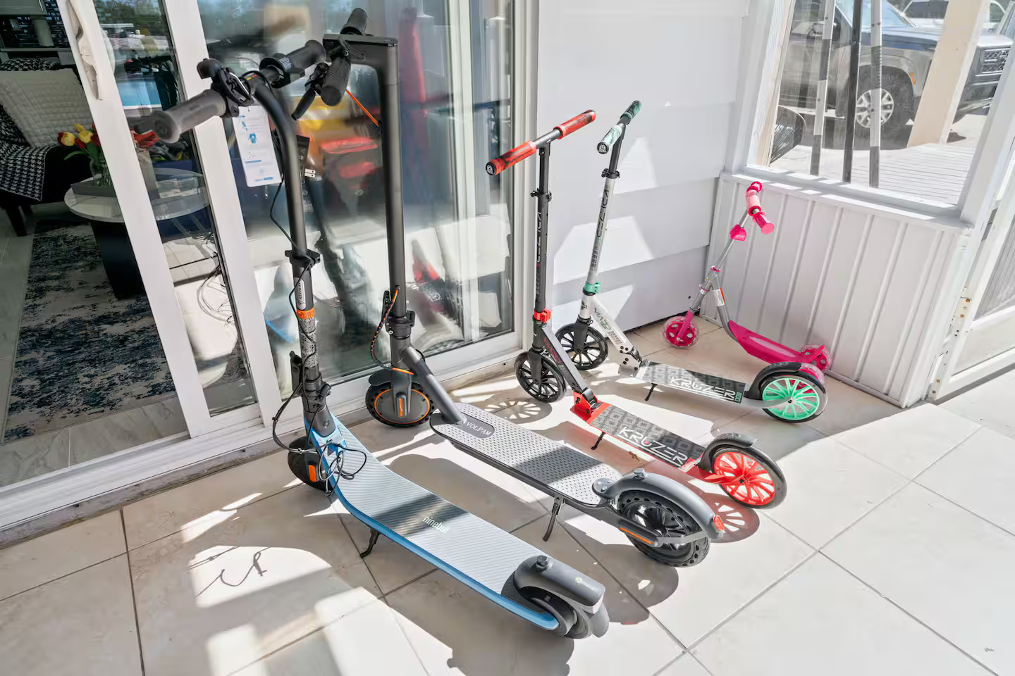 A group of electric scooters are sitting on a patio next to a sliding glass door.