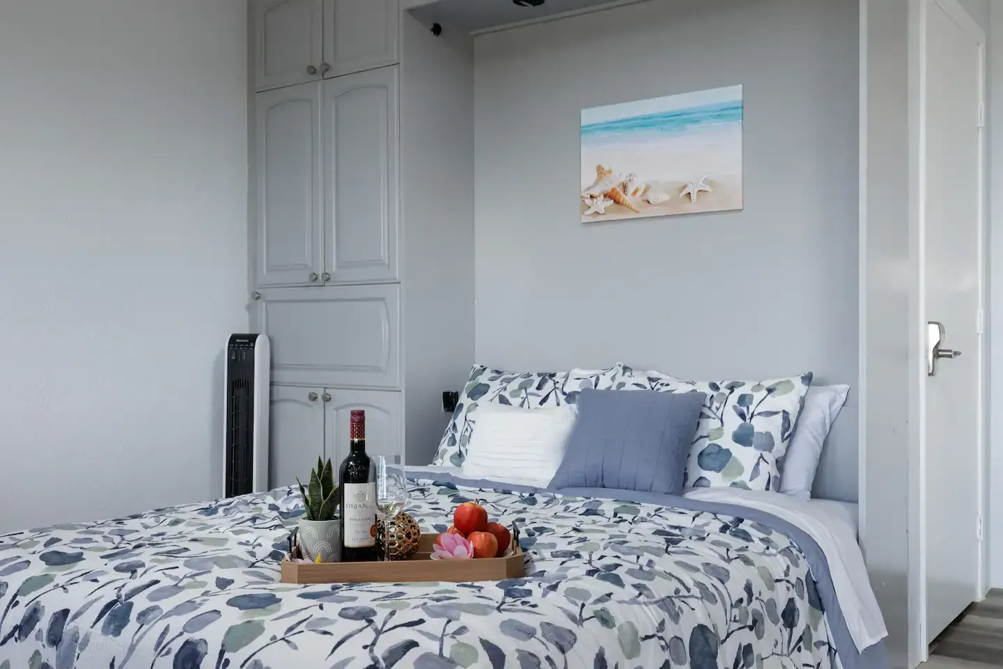 A bed with a tray of food and a bottle of wine on it in a bedroom.