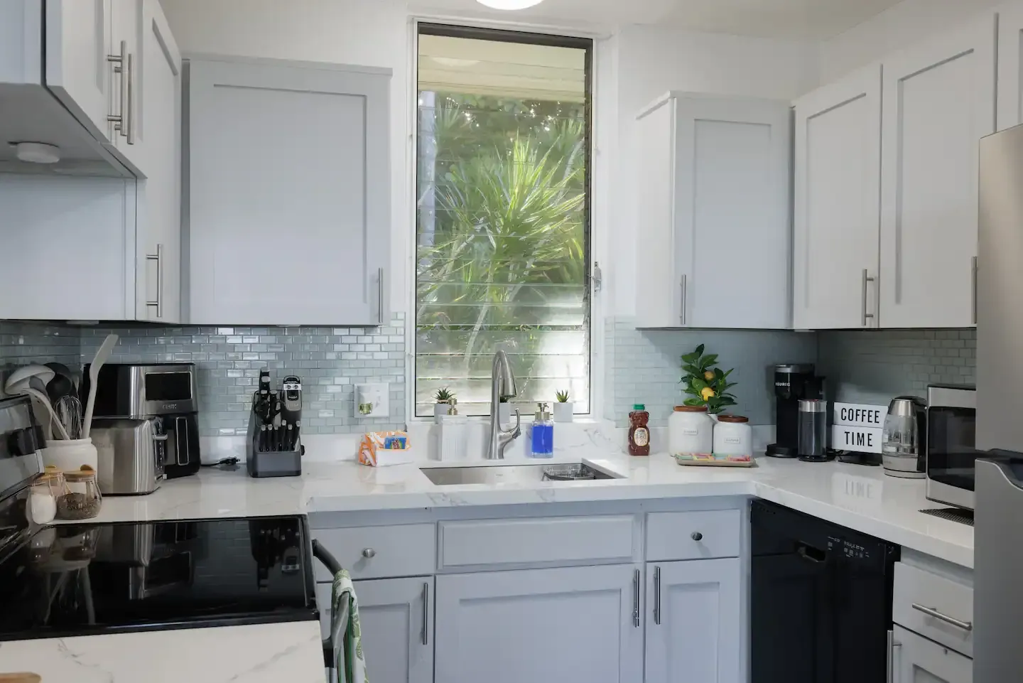 A kitchen with white cabinets , a sink , a stove , and a window.