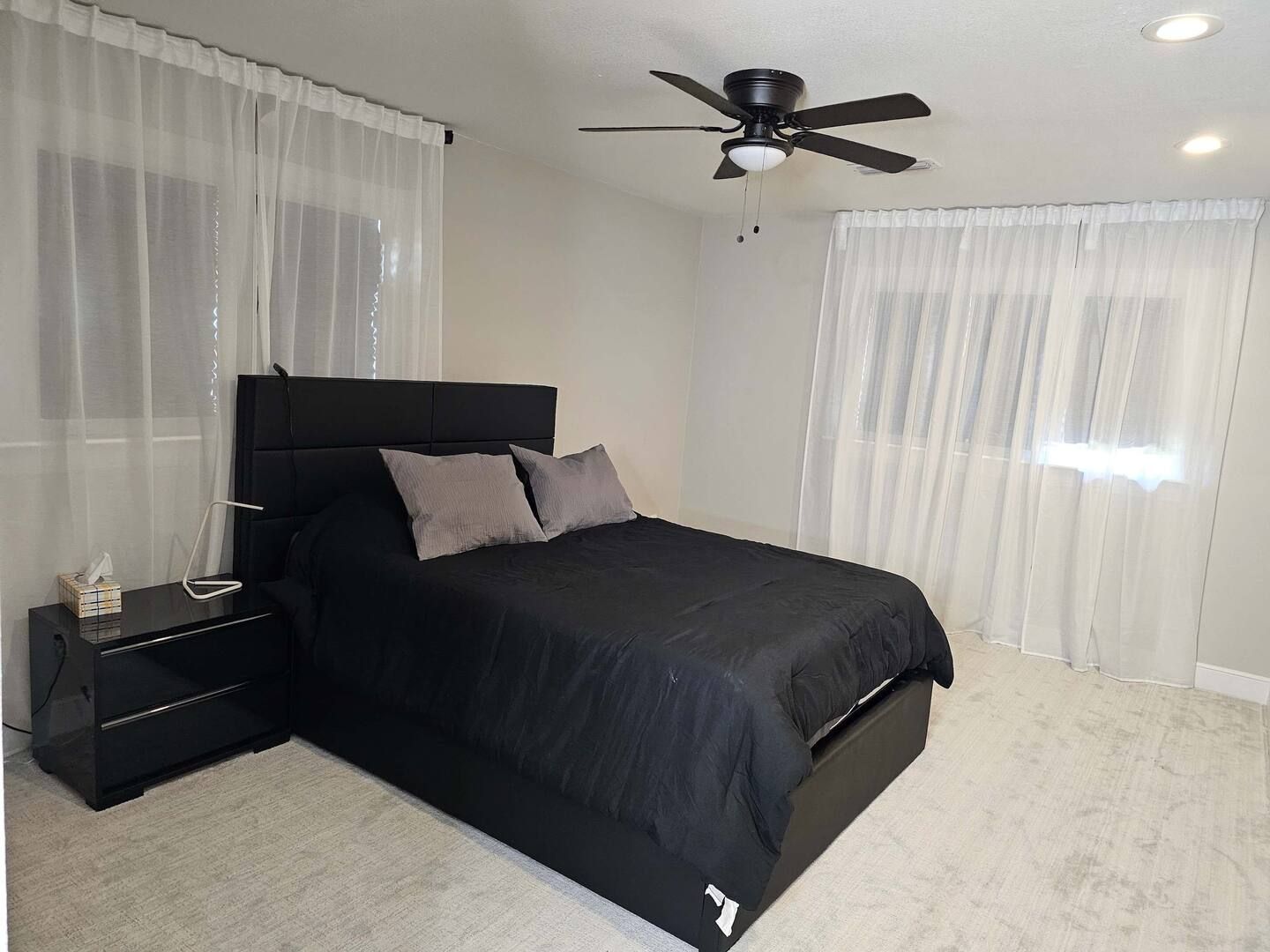 A bedroom with a black bed and a ceiling fan