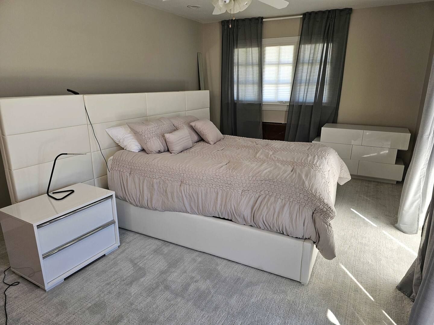 A bedroom with a bed , nightstand , dresser and window.