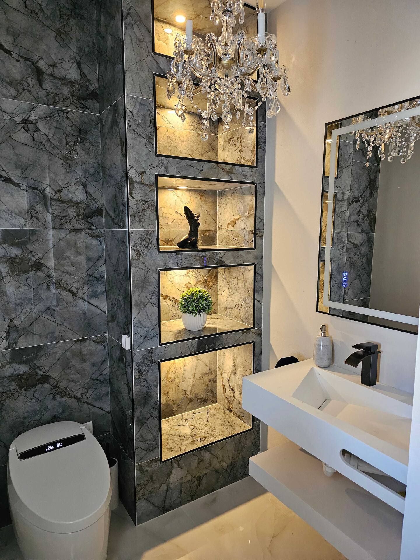 A bathroom with a toilet , sink , mirror and chandelier.
