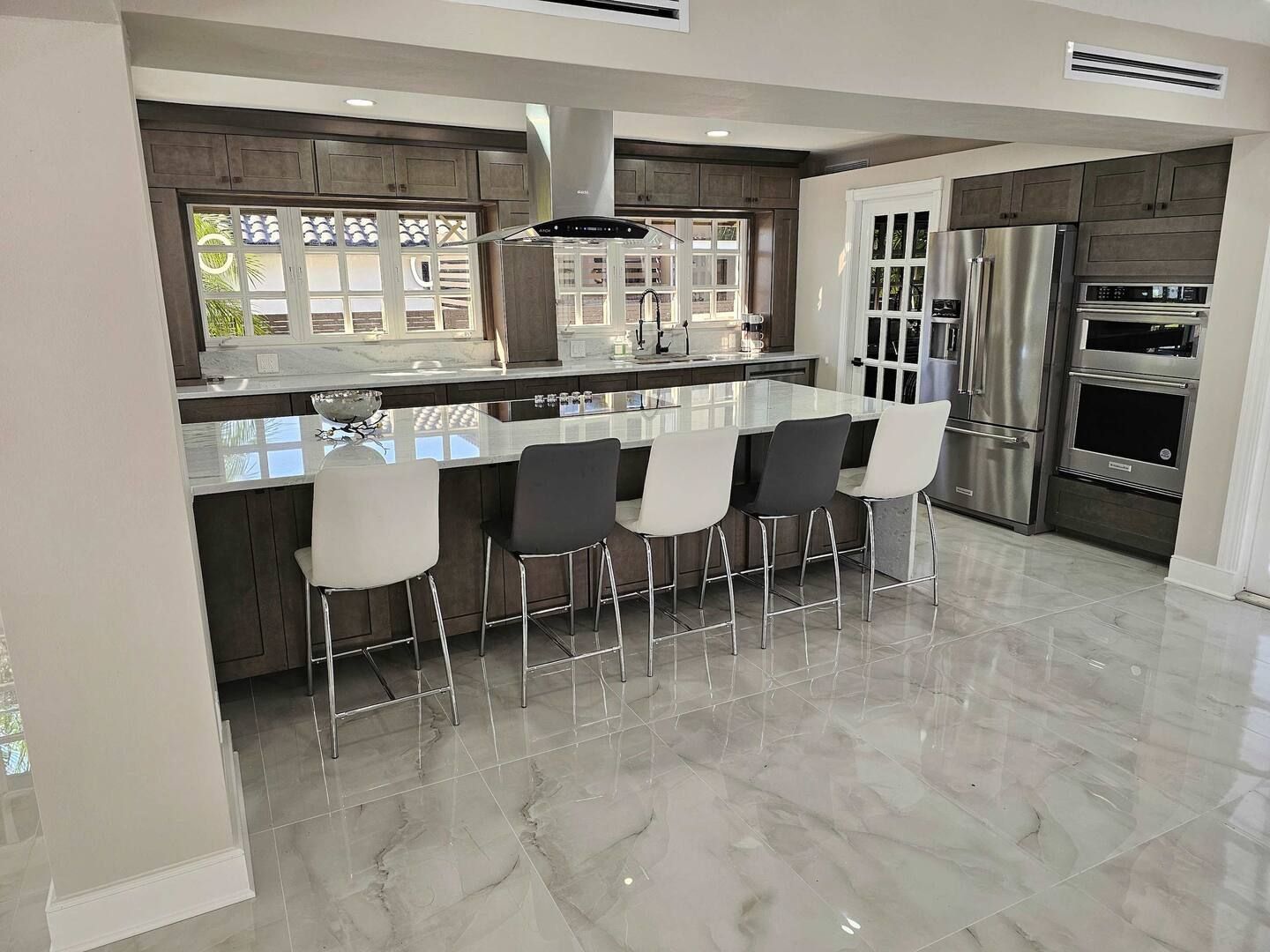 A kitchen with a long counter and stools and a refrigerator.