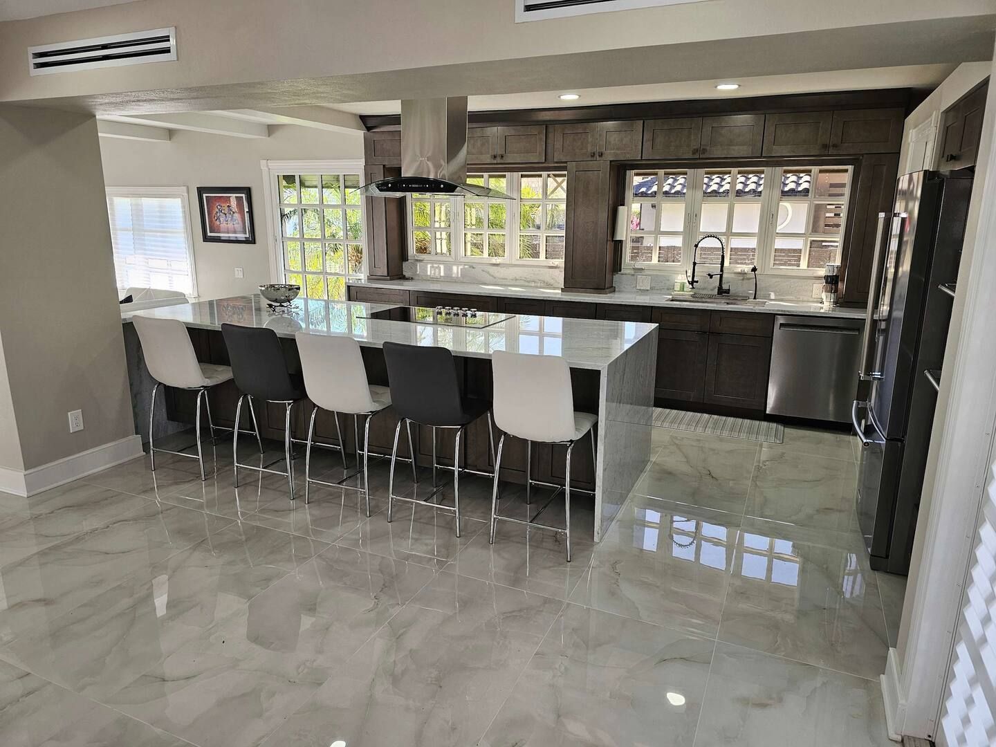 A kitchen with a large island , stools and a refrigerator.